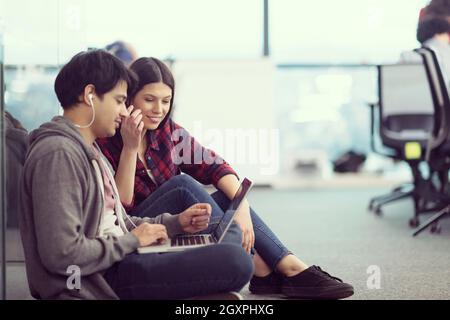 young software developers couple using laptop computer writing programming code while sitting on the floor at modern creative startup office Stock Photo