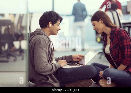 young software developers couple using laptop computer writing programming code while sitting on the floor at modern creative startup office Stock Photo