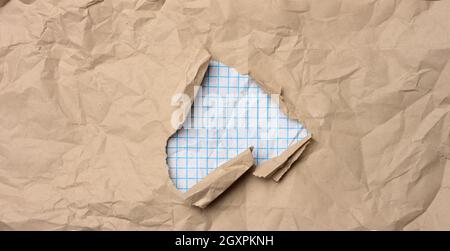 brown kraft paper with a hole in which there are torn edges, the middle is white squared paper Stock Photo