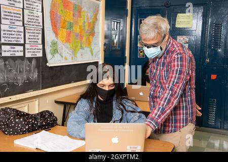 Education High School classroom scene male teacher working with female student in classroom, both wearing face masks to protect vs Covid-19 Stock Photo
