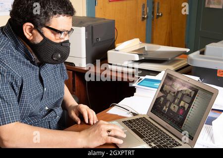 Education High School male teacher in face mask conducting class via Zoom on laptop computer during the Covid-19 pandemic Stock Photo