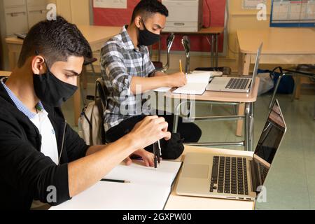 Education High School classroom scene two male students working in class, one using protractor, both with laptop computers on desks in front of them Stock Photo
