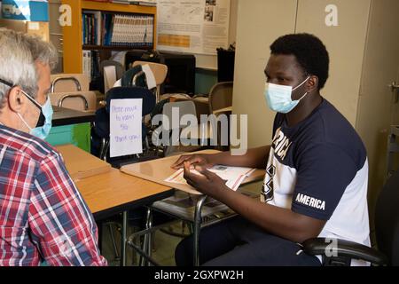 Education High School classroom scene male teacher talking with male student, both wearing face masks to protect against Covid-19 infection Stock Photo