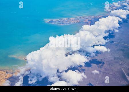 Airplane view of large white clouds over land against ocean coast Stock Photo