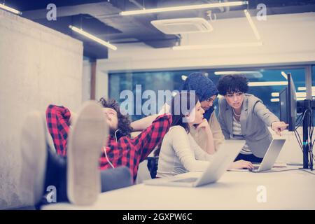 young software developer resting with legs on desk while his multiethnics business team writing programming code in the background at startup office Stock Photo
