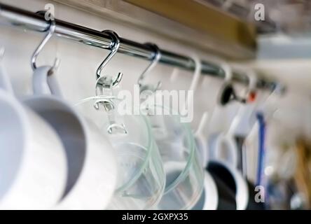 A set of mugs hanging on hooks in a modern home kitchen. Everyday objects. Domestic life. Stock Photo