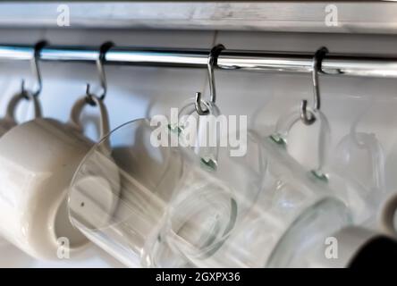 A set of mugs hanging on hooks in a modern home kitchen. Everyday objects. Domestic life. Stock Photo