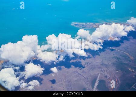 Large white clouds from airplane over land with colorful ocean view Stock Photo
