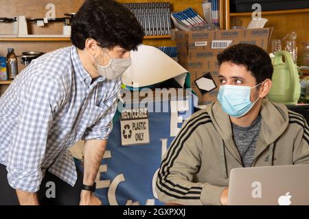 Education High School classroom scene, male teacher listening to male student, both wearing face masks to protect against Covid-19 infection Stock Photo
