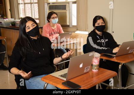 Education High School classroom scene female student talking using hand gestures classmates listening, all wearing face masks to protect against Covid Stock Photo
