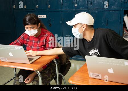 Education High School classroom scene male student leaning over to explain something to his neigbor, both wearing face masks to protect against Covid Stock Photo