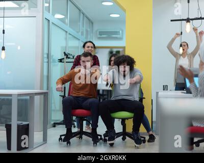business people having fun while racing on office chairs in modern coworking open space office Stock Photo
