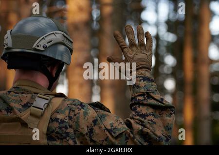 modern warfare soldier officer is  showing tactical hand signals to silently give orders and alers for squad team forest enviroment Stock Photo