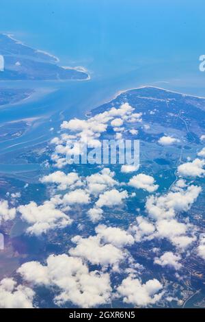 Airplane view of land with small white clouds and blue water Stock Photo