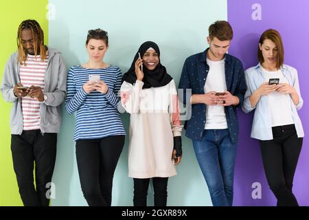 a group of diverse teenagers use mobile devices while posing for studio photography Stock Photo