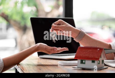 real estate agent holding house key to his client after signing contract agreement in office,concept for real estate, moving home or renting property. Stock Photo