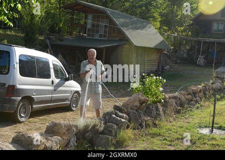 Senior gardener watering the plants using a rubber hose in sunset Stock Photo