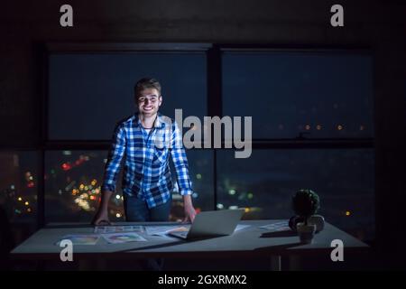portrait of young male engineer on construction site checking documents and business workflow using laptop computer in new startup office at night Stock Photo
