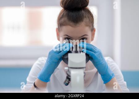 Young female student scientist looking through a microscope while doing some research in the laboratory Stock Photo