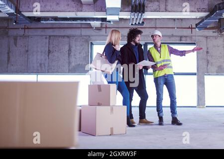 architect using tablet computer while showing house design plans to a young couple at construction site Stock Photo