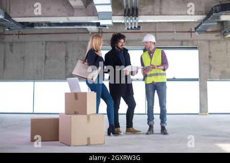 architect using tablet computer while showing house design plans to a young couple at construction site Stock Photo
