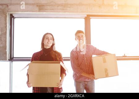 happy young casual business team carrying cardboard boxes with sunlight through the windows during moving in at new unfinished startup office building Stock Photo