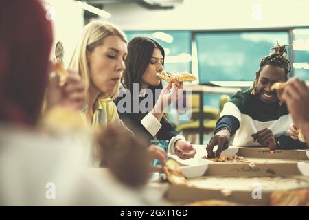 Friendly diverse multiethnic business team eating sharing pizza together in startup office, multiracial coworkers staff group enjoying break talking l Stock Photo