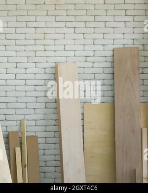 Wood planks of various sizes lean on a white brick wall. Morning work atmosphere in the workshop room. Stock Photo