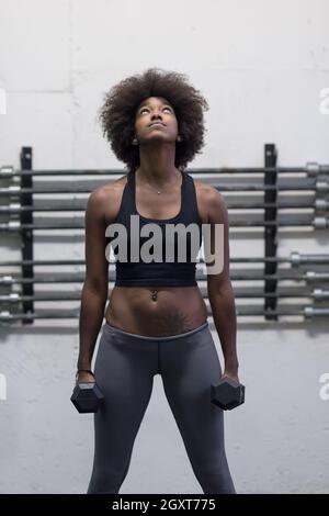 young beautiful African American woman doing bicep curls in a gym Stock Photo