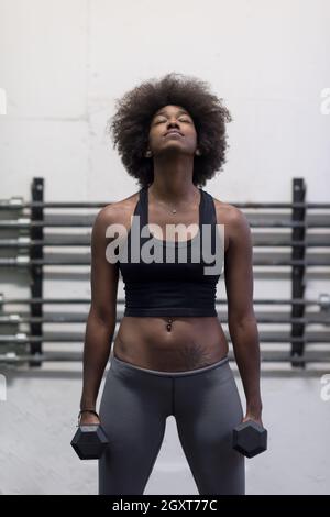 young beautiful African American woman doing bicep curls in a gym Stock Photo