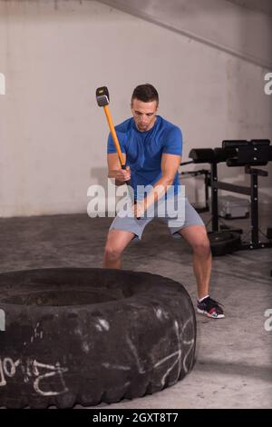 Sledgehammer Tire Hits young muscular man workout at gym with hammer and tractor tire Stock Photo