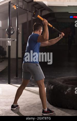 Sledgehammer Tire Hits young muscular man workout at gym with hammer and tractor tire Stock Photo