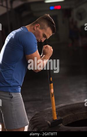 Sledgehammer Tire Hits young muscular man workout at gym with hammer and tractor tire Stock Photo