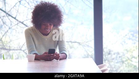 Handsome young african american woman drinking coffee and using a mobile phone at  home Stock Photo
