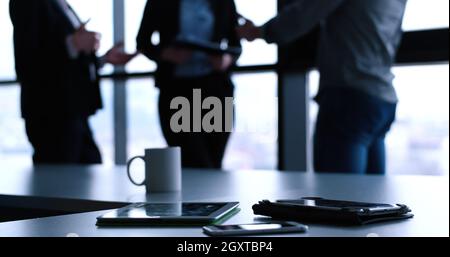 Devices on table with business people in background in modern office building Stock Photo