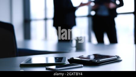Devices on table with business people in background in modern office building Stock Photo