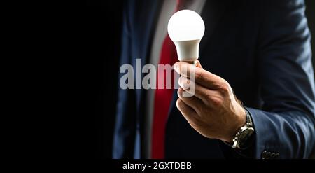 A businessman in a black suit is holding a light bulb in his hand illuminated on a black background with copy space. business growth idea business ide Stock Photo