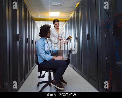 Team of young technicians working together on servers at the data center using laptop computer Stock Photo