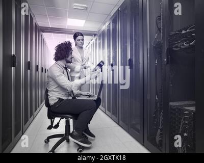 Team of young technicians working together on servers at the data center using laptop computer Stock Photo