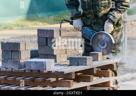 A worker with a circular saw cuts paving slabs in close-up. Stock Photo