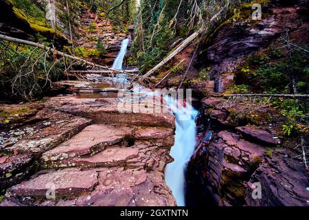 Water rushing through deep gorge with red rocks and waterfall in background Stock Photo