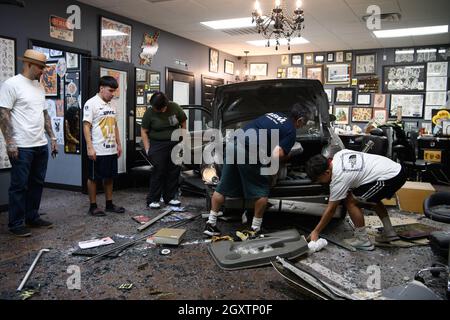 October 5, 2021: A car slammed into the Stainless Studios - Custom Tattoo Parlor in Dallas TX after being struck by another car, destroying a customer sitting area and tattoo station.None of the shop's employees or the occupants of the car were injured. The shop manager said that if a customer had not cancelled her appointment for this evening, they would have been sitting in that station when the vehicle struck.The other car fled the scene, minus a bumper, and is being sought by the Dallas Police Department. The occupants of the errant vehicle take personal items out of the car befor Stock Photo