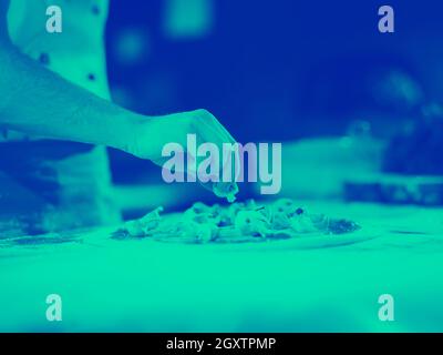 chef putting fresh mushrooms over pizza dough on kitchen table Stock Photo