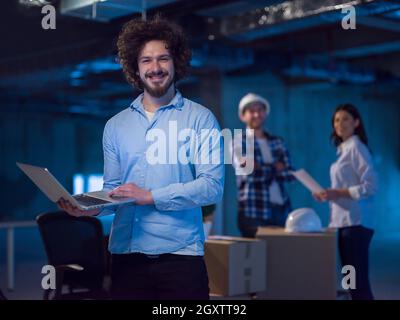 young male architect on construction site checking documents and business workflow using laptop computer with colleagues in the background in new star Stock Photo