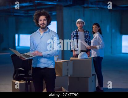 young male architect on construction site checking documents and business workflow using laptop computer with colleagues in the background in new star Stock Photo