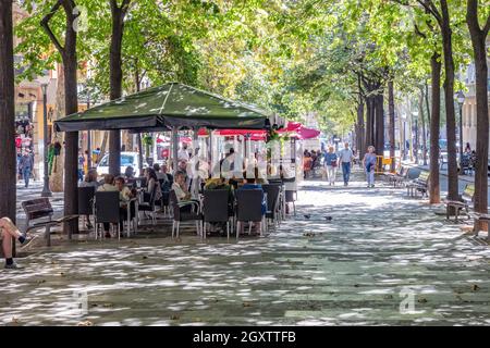 Barcelona, Spain - September 19, 2021: View of Some people walking along the Ramblas in Barcelona (boulevard) and others having a drink on the terrace Stock Photo