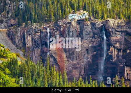 Close up of waterfall on large vertical cliff with house at top Stock Photo