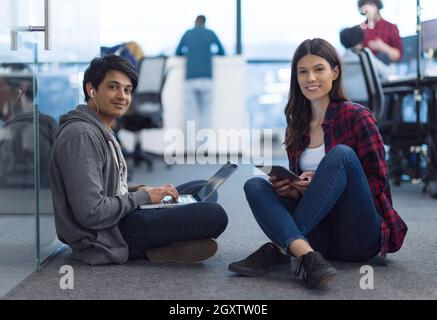 young software developers couple using laptop and tablet computer writing programming code while sitting on the floor at modern creative startup offic Stock Photo