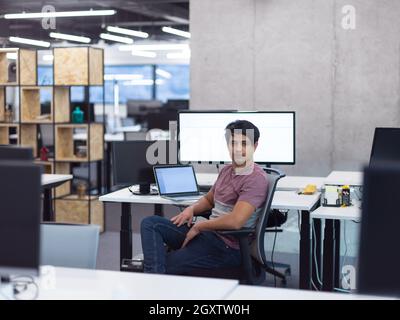 Portrait of young indian successful male software developer sitting on desk at modern startup office Stock Photo