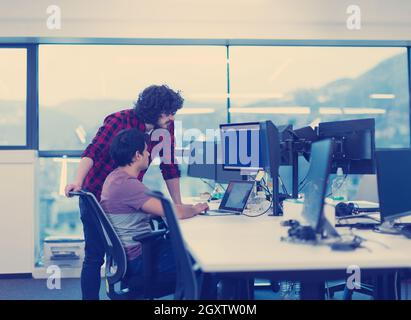 two young male software developers using laptop and desktop computer while writing programming code at modern creative startup office Stock Photo